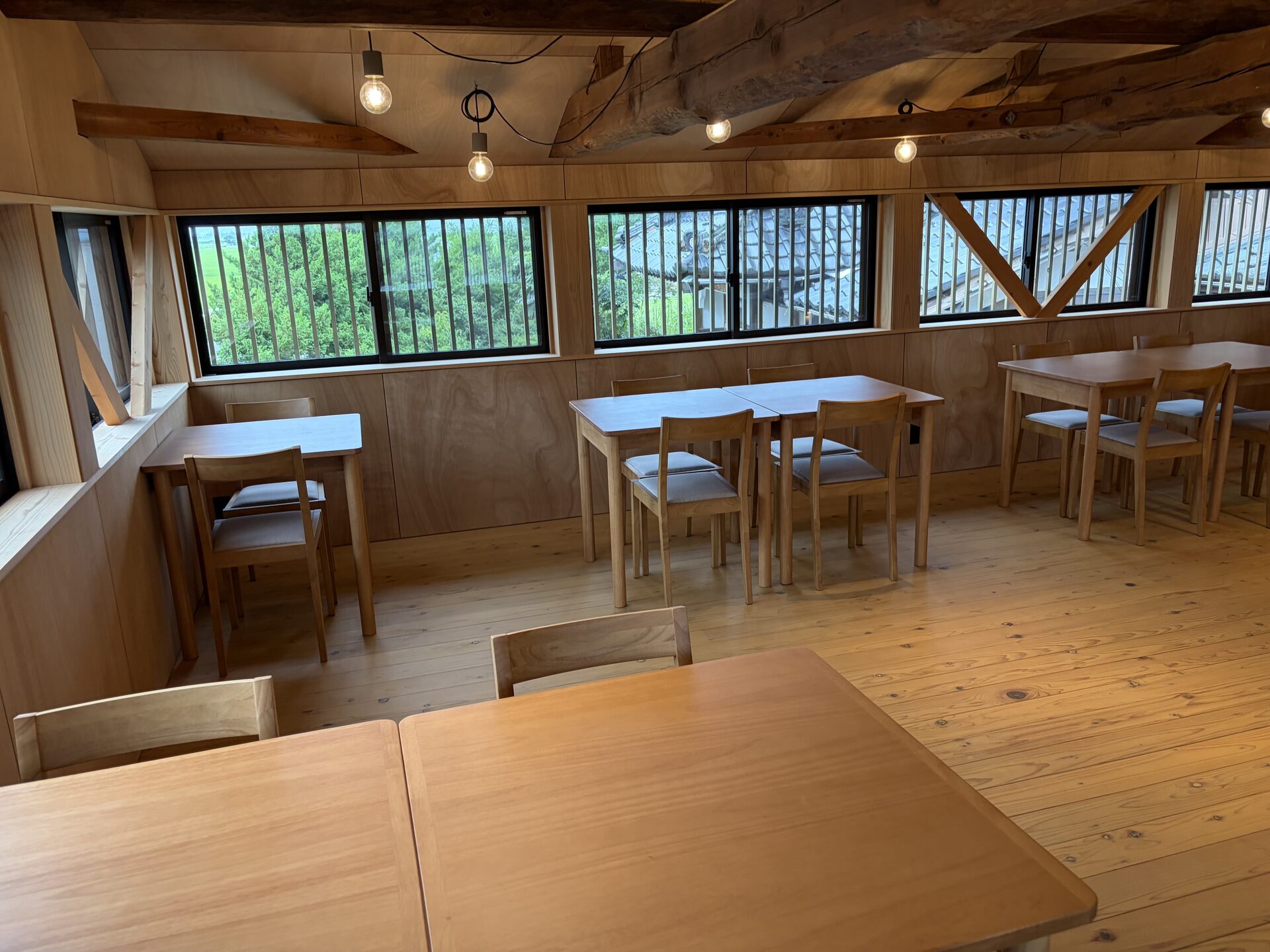 Restored kominka dining room with wooden tables and seating beside large windows